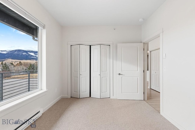 unfurnished bedroom featuring a mountain view, light colored carpet, a baseboard heating unit, baseboards, and a closet