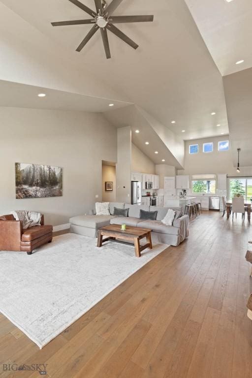 living room featuring ceiling fan, a towering ceiling, and light wood-type flooring