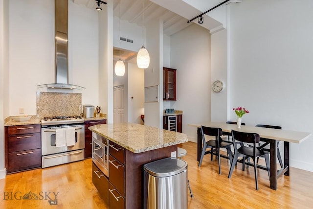 kitchen featuring hanging light fixtures, wall chimney range hood, decorative backsplash, a kitchen island, and appliances with stainless steel finishes