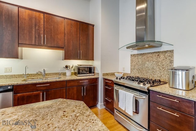 kitchen featuring light stone counters, wall chimney exhaust hood, stainless steel appliances, sink, and light hardwood / wood-style floors