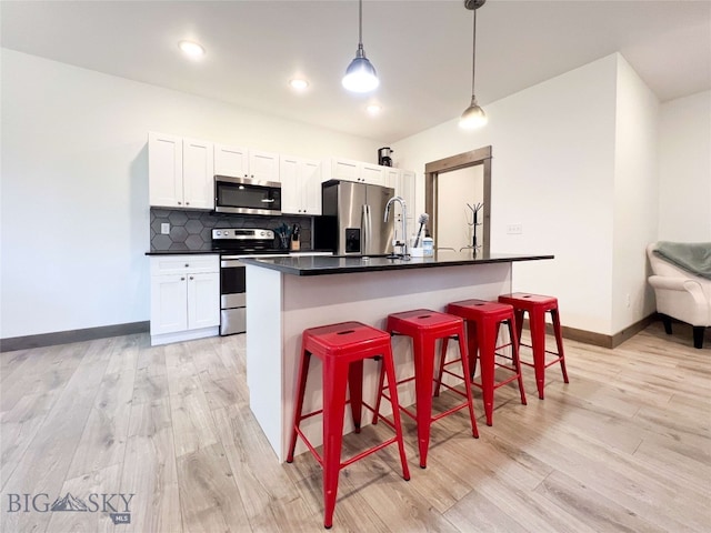 kitchen featuring a breakfast bar, a kitchen island with sink, white cabinets, hanging light fixtures, and stainless steel appliances