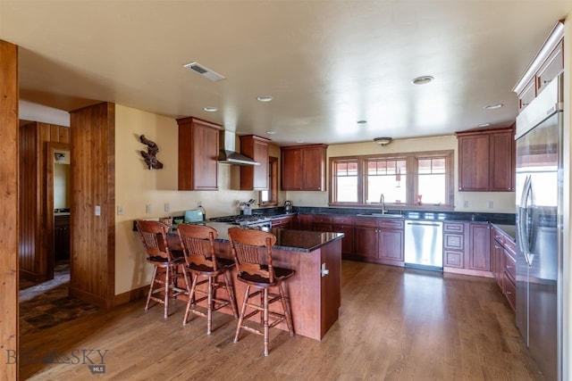 kitchen with visible vents, appliances with stainless steel finishes, a sink, a peninsula, and wall chimney exhaust hood