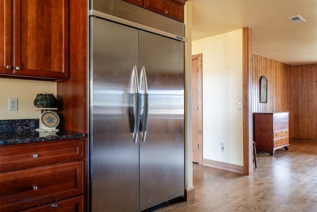 kitchen with light wood finished floors, visible vents, dark stone countertops, stainless steel built in fridge, and wood walls