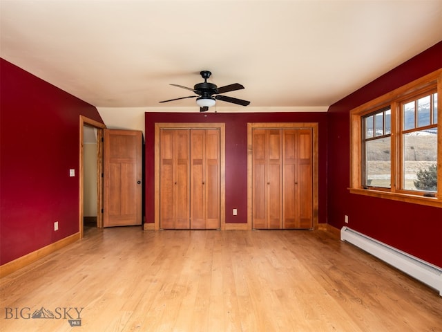 unfurnished bedroom featuring baseboard heating, multiple closets, light wood-style flooring, and baseboards