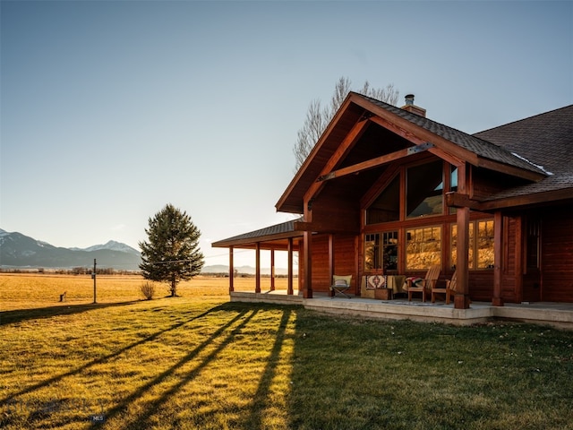 back of property with a rural view, a chimney, a mountain view, and a yard