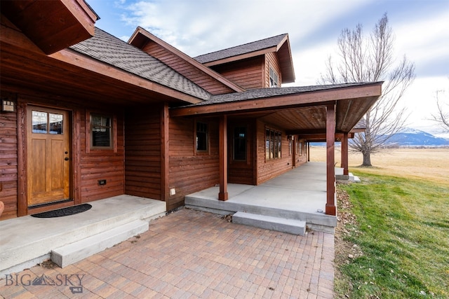 doorway to property featuring a shingled roof, a yard, and a mountain view