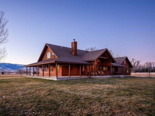 back house at dusk with a mountain view and a lawn