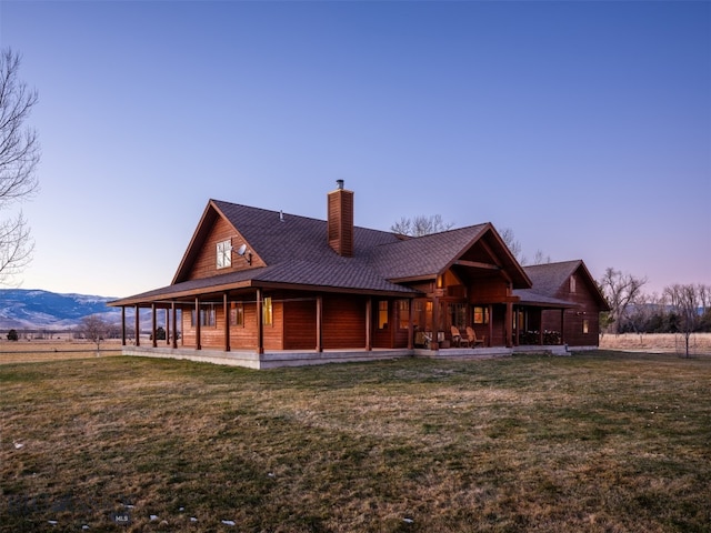 rear view of house with a mountain view, a porch, a chimney, and a lawn