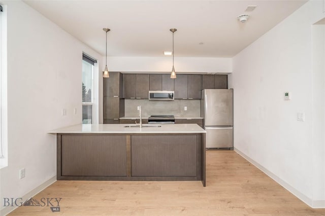 kitchen with sink, stainless steel appliances, kitchen peninsula, decorative light fixtures, and dark brown cabinets