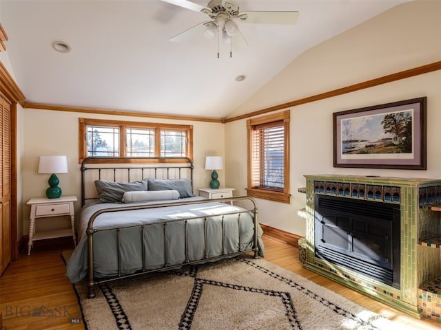 bedroom featuring light hardwood / wood-style flooring, ceiling fan, lofted ceiling, and a tiled fireplace