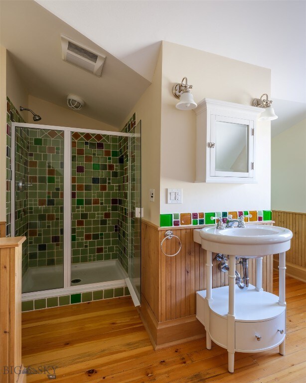 bathroom with hardwood / wood-style flooring, vaulted ceiling, and a shower with shower door