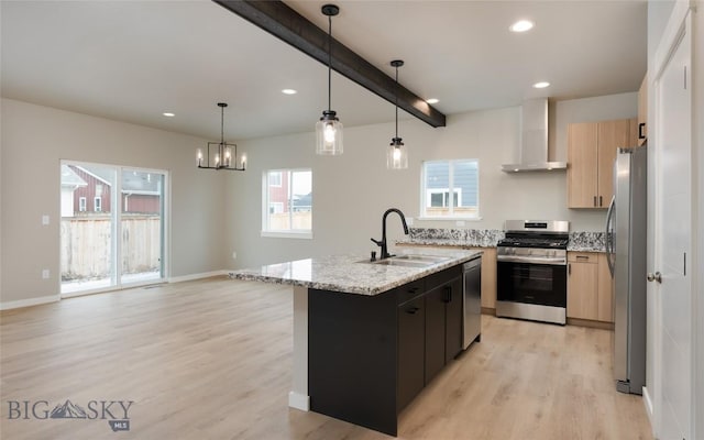 kitchen with a sink, light wood-style floors, appliances with stainless steel finishes, wall chimney exhaust hood, and an island with sink