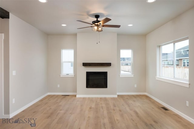 unfurnished living room featuring light wood-style floors, recessed lighting, a glass covered fireplace, and baseboards