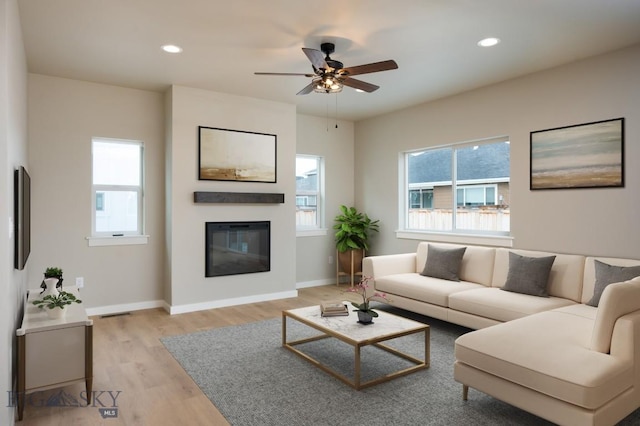 living area featuring baseboards, a ceiling fan, a glass covered fireplace, light wood-style floors, and recessed lighting