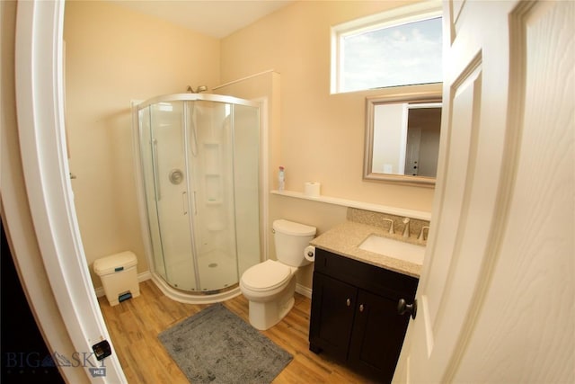 bathroom with toilet, a stall shower, vanity, wood finished floors, and baseboards