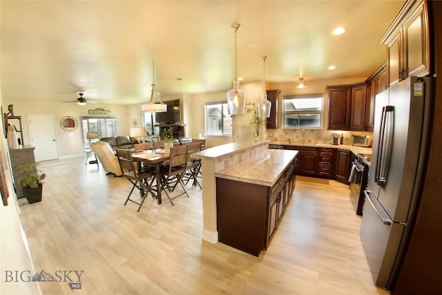 kitchen featuring open floor plan, a center island, decorative light fixtures, freestanding refrigerator, and light wood-style floors