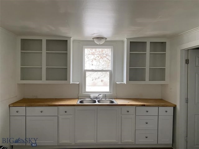 kitchen featuring butcher block counters, sink, white cabinets, and built in features