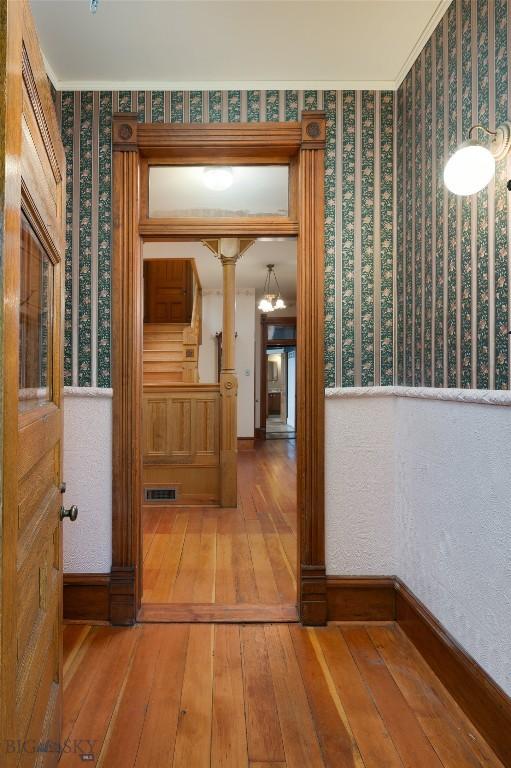 corridor featuring hardwood / wood-style flooring, ornamental molding, and an inviting chandelier