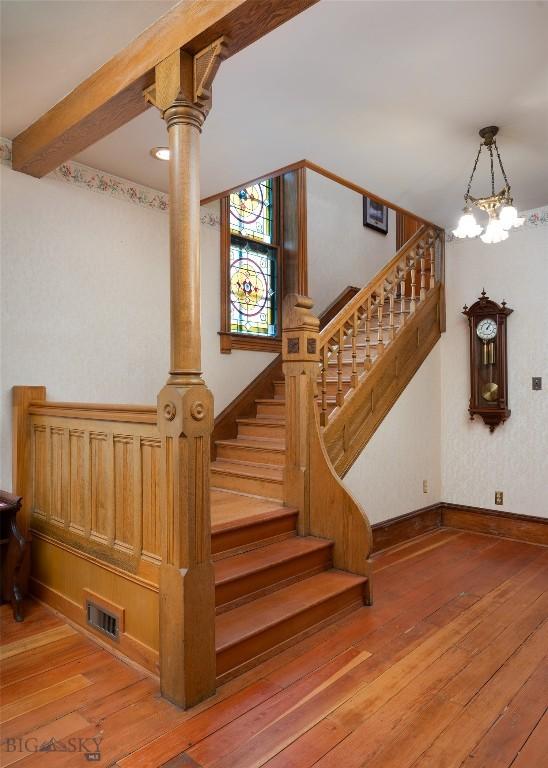 stairway with beamed ceiling, wood-type flooring, and a chandelier