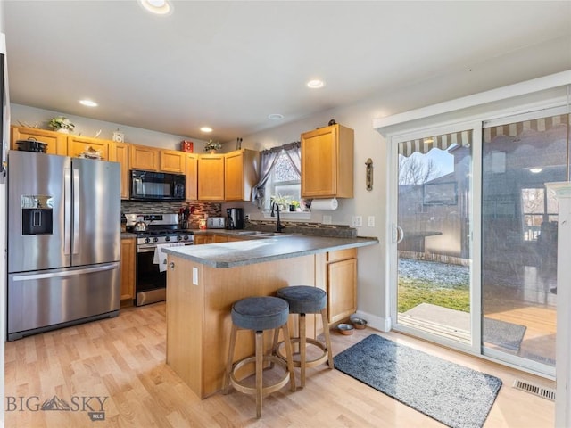 kitchen with sink, stainless steel appliances, kitchen peninsula, a kitchen bar, and light wood-type flooring