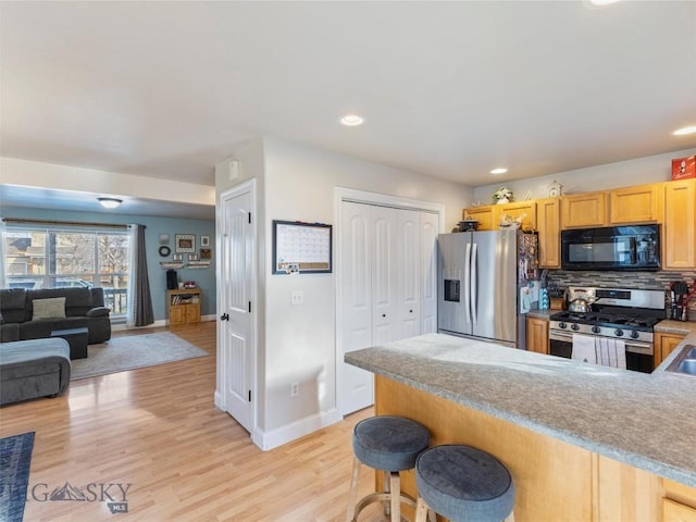 kitchen featuring decorative backsplash, appliances with stainless steel finishes, light brown cabinetry, a breakfast bar, and light hardwood / wood-style floors