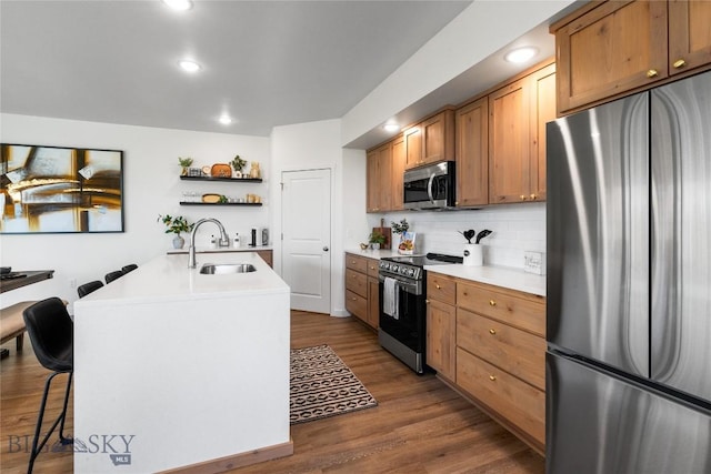 kitchen featuring appliances with stainless steel finishes, dark hardwood / wood-style flooring, backsplash, a kitchen island with sink, and sink