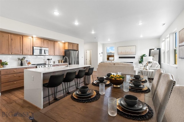 kitchen with sink, a kitchen island with sink, stainless steel fridge, decorative backsplash, and a breakfast bar