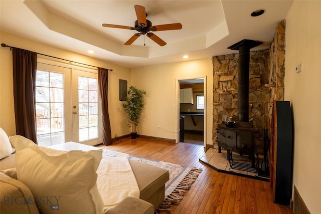 living room with ceiling fan, wood-type flooring, a wood stove, and a tray ceiling