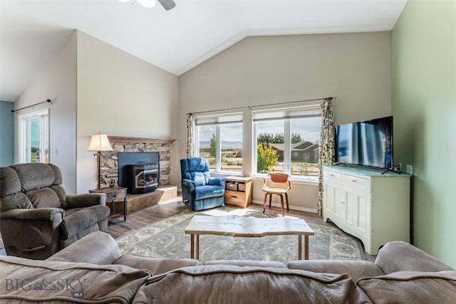 living room with ceiling fan, light wood-type flooring, a wood stove, and vaulted ceiling