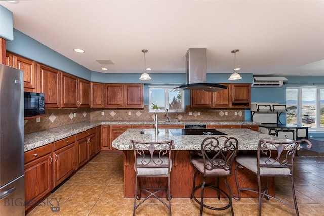 kitchen with island exhaust hood, pendant lighting, light stone countertops, and a kitchen island with sink