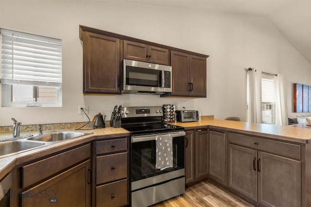 kitchen with kitchen peninsula, stainless steel appliances, sink, light hardwood / wood-style flooring, and lofted ceiling