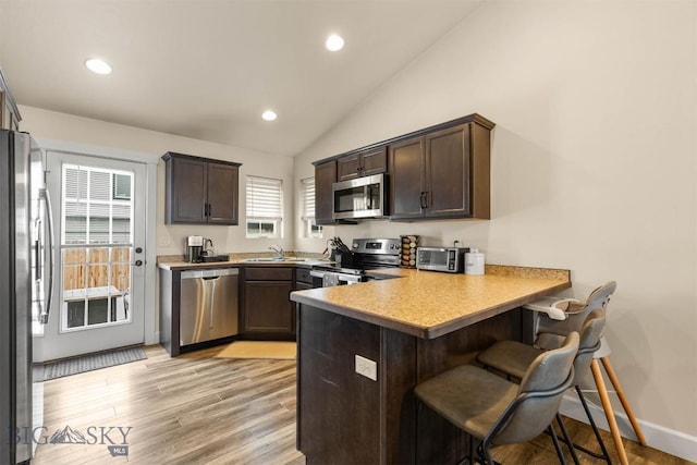 kitchen featuring kitchen peninsula, appliances with stainless steel finishes, a breakfast bar, light hardwood / wood-style flooring, and lofted ceiling