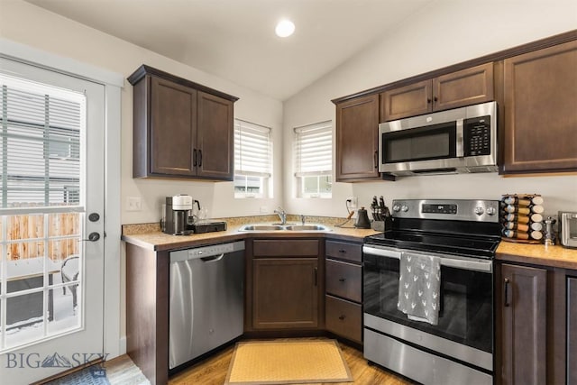 kitchen with sink, light hardwood / wood-style flooring, vaulted ceiling, dark brown cabinetry, and stainless steel appliances