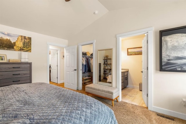 bedroom featuring connected bathroom, a spacious closet, light hardwood / wood-style floors, vaulted ceiling, and a closet