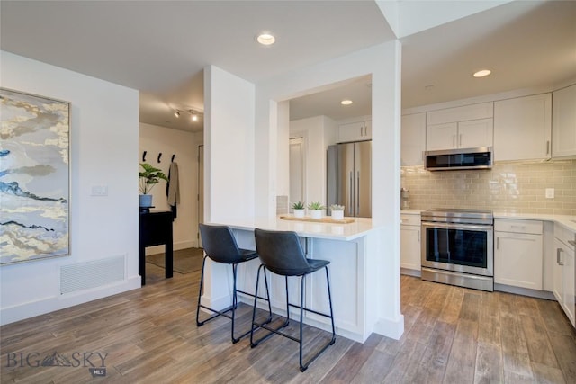 kitchen with a kitchen breakfast bar, light wood-type flooring, tasteful backsplash, stainless steel appliances, and white cabinetry