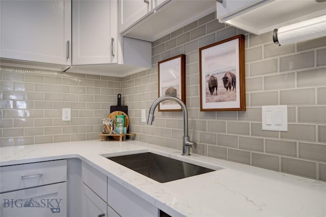 kitchen with backsplash, light stone countertops, sink, and white cabinets