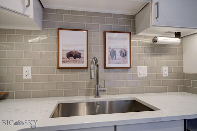 kitchen featuring light stone countertops, tasteful backsplash, white cabinets, and sink