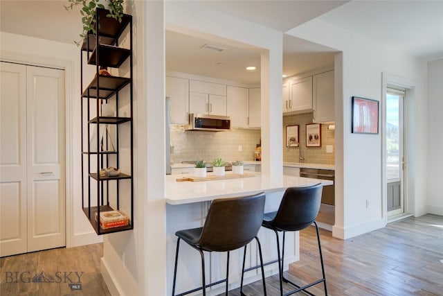 kitchen with stainless steel appliances, tasteful backsplash, light hardwood / wood-style flooring, a breakfast bar area, and white cabinets