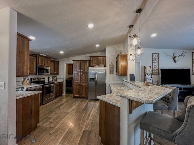 kitchen with a kitchen bar, decorative light fixtures, appliances with stainless steel finishes, kitchen peninsula, and light stone countertops