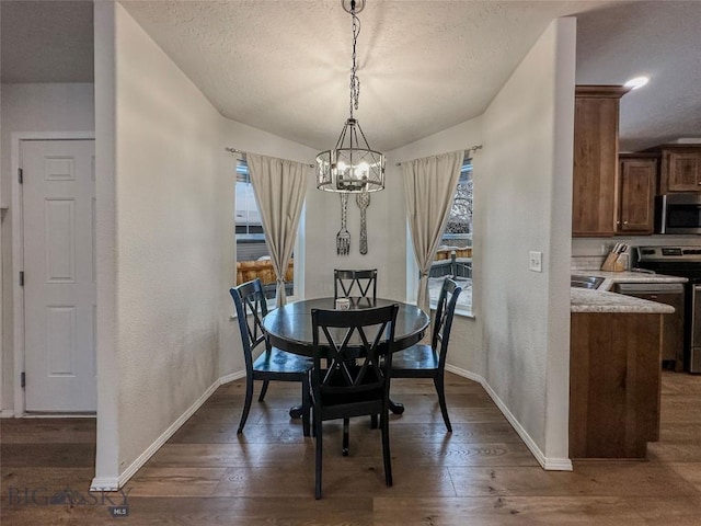 dining room featuring a textured ceiling, dark wood-type flooring, a chandelier, and a healthy amount of sunlight