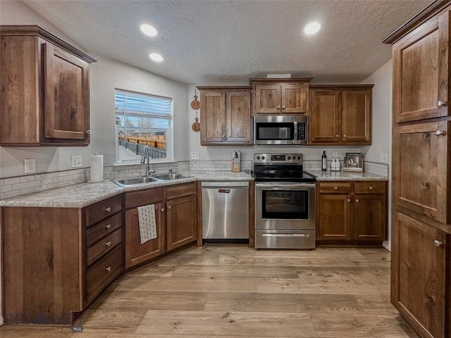 kitchen with appliances with stainless steel finishes, sink, a textured ceiling, and light hardwood / wood-style flooring