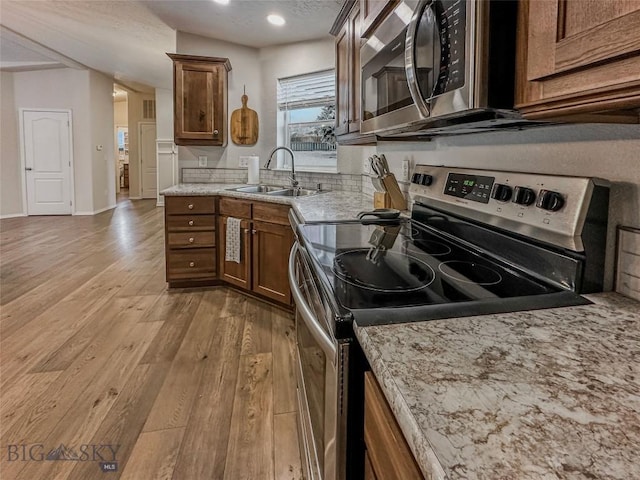 kitchen with stainless steel appliances, light stone countertops, sink, and light wood-type flooring