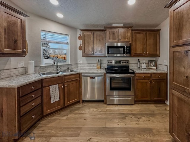 kitchen with appliances with stainless steel finishes, sink, light hardwood / wood-style flooring, and a textured ceiling