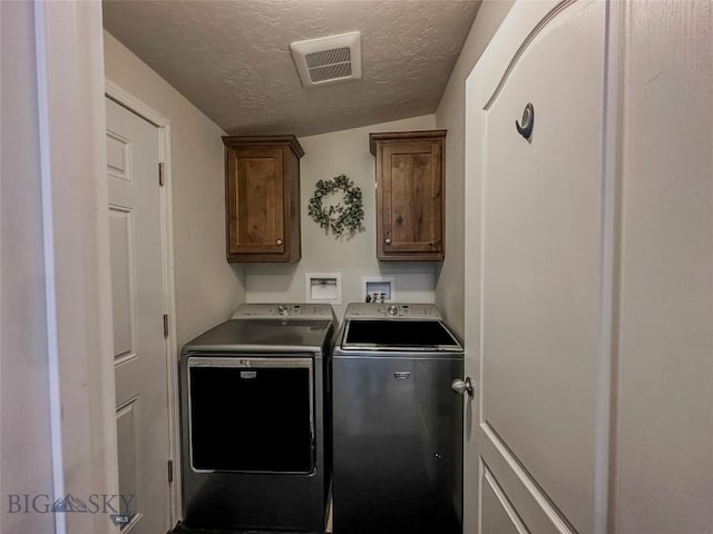 clothes washing area with cabinets, washer and clothes dryer, and a textured ceiling