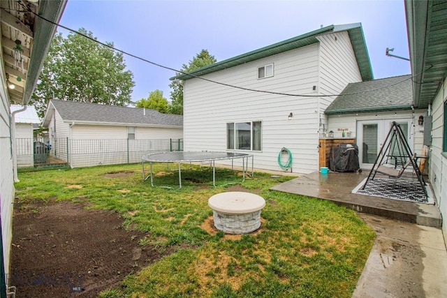 rear view of property featuring a patio, a trampoline, a fire pit, and a lawn