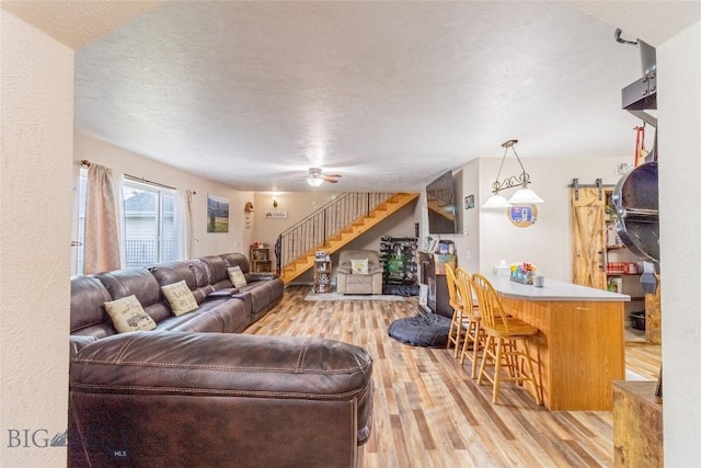 living room featuring a barn door, ceiling fan, light hardwood / wood-style floors, and a textured ceiling