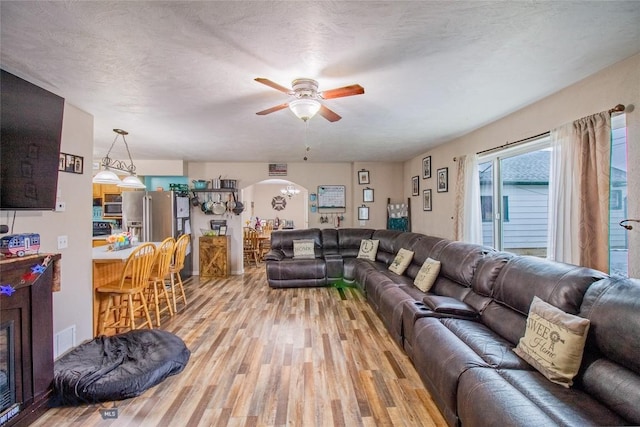 living room with ceiling fan, a textured ceiling, and light wood-type flooring