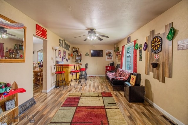 living room with bar area, ceiling fan, and hardwood / wood-style floors