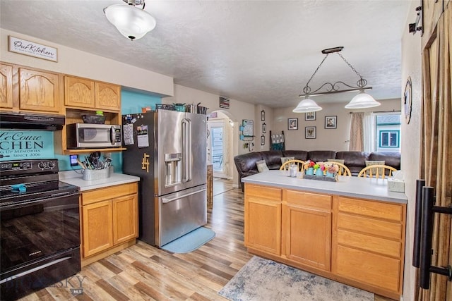 kitchen with pendant lighting, light hardwood / wood-style flooring, a barn door, a textured ceiling, and appliances with stainless steel finishes