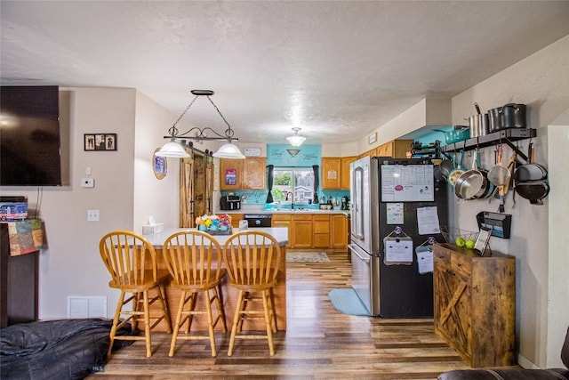 kitchen with a textured ceiling, sink, wood-type flooring, black dishwasher, and stainless steel refrigerator